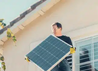 A Man in Black Shirt Standing on the Roof while Holding a Solar Panel