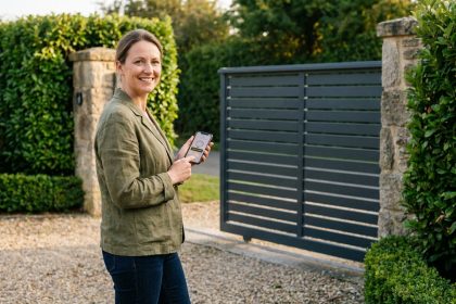 Femme utilisant son smartphone pour contrôler un portail automatique coulissant devant une maison résidentielle