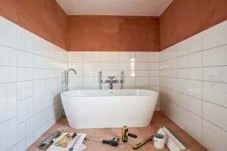 Vue d'ensemble d'une salle de bain en cours de rénovation dans l'Hérault avec carrelage blanc, baignoire îlot et outils de plomberie