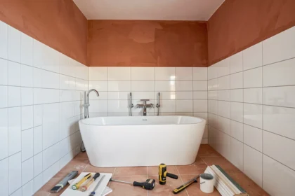 Vue d'ensemble d'une salle de bain en cours de rénovation dans l'Hérault avec carrelage blanc, baignoire îlot et outils de plomberie