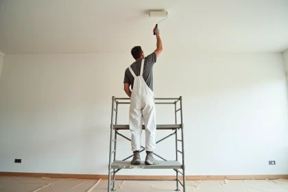 Peintre professionnel appliquant de la peinture blanche au rouleau sur un plafond de 50m2 dans un appartement vide